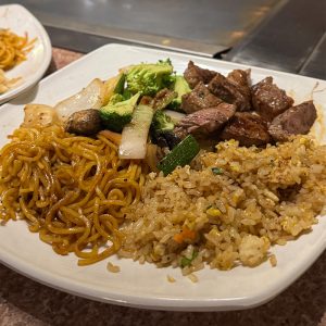 Mixed Asian cuisine with fried rice, stir-fried noodles, beef, and vegetables on a white plate.