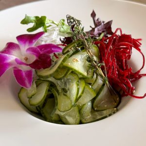 Fresh cucumber salad garnished with edible flowers and herbs on a white plate.