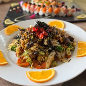 Vegetable stir-fry with seaweed and orange slices on a white plate.