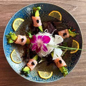 Elegant sushi rolls with lemon slices and edible flowers on a blue ceramic plate.
