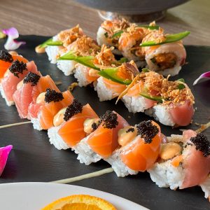 Assorted sushi rolls with fish, caviar, and garnishes on a black plate.