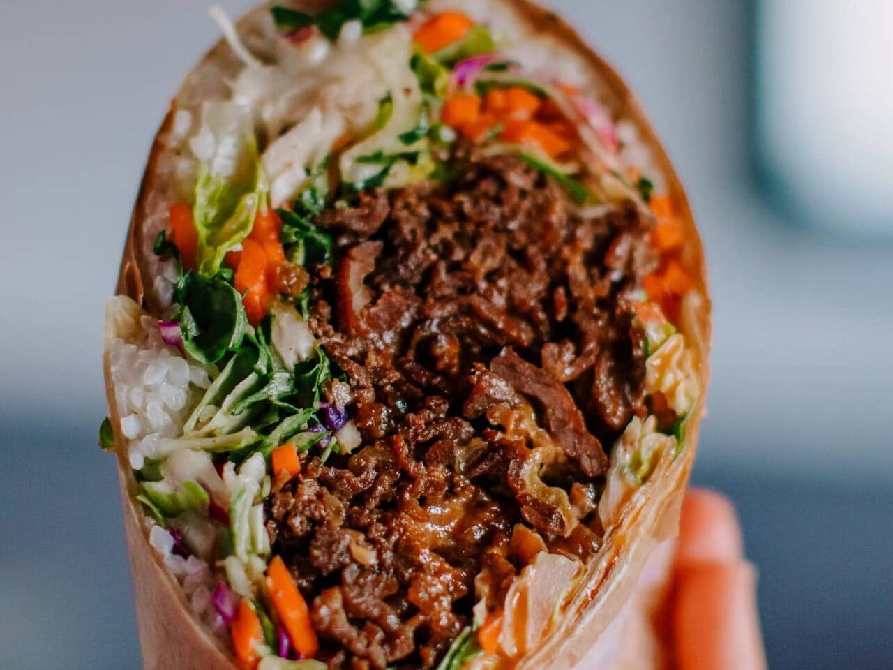 Close-up of a beef taco with fresh vegetables and sauce in a soft tortilla.