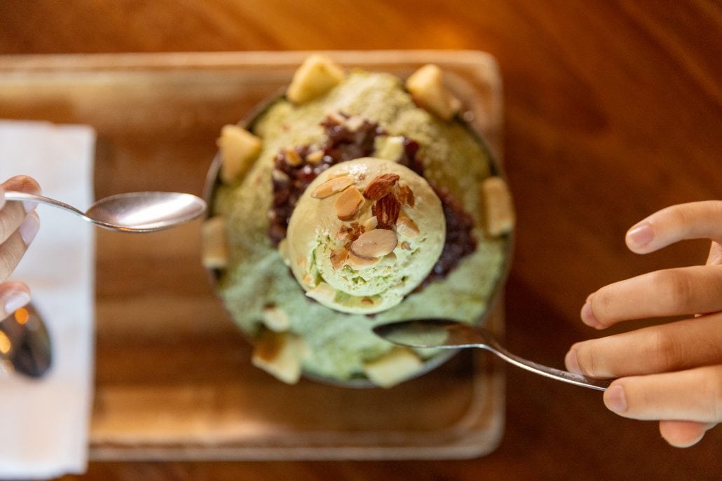 Close-up of a green ice cream scoop with almonds on top, on a wooden table.
