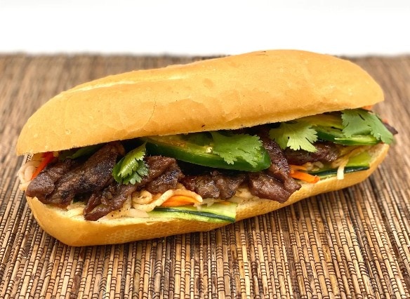 Delicious beef pho sandwich with fresh herbs and vegetables on a wooden surface.
